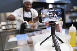 Close-up photo of man cooking dessert at the kitchen and filming himself on video on the phone